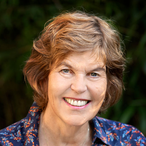 Sympathische Frau mit Blumenmuster-Bluse vor unscharfem, gr&uuml;nem Hintergrund